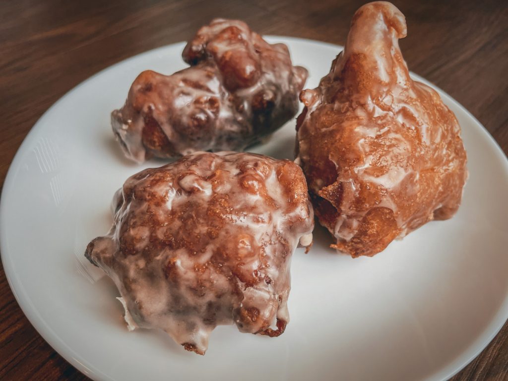 three gluten free apple fritters glazed with cinnamon vanilla icing on a white plate
