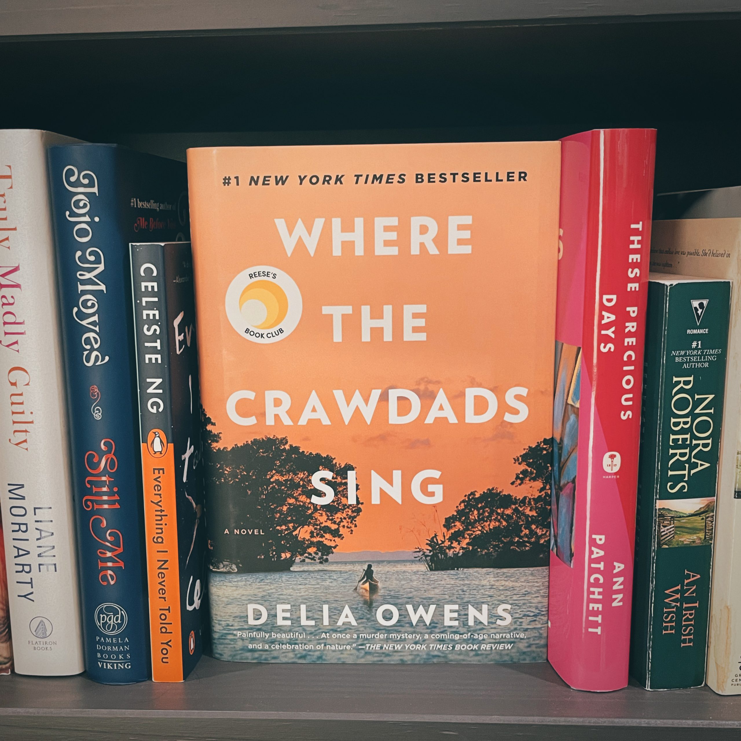 close up of the cover of Where the Crawdads Sing book by Delia Owens on a shelf with other books on either side of it