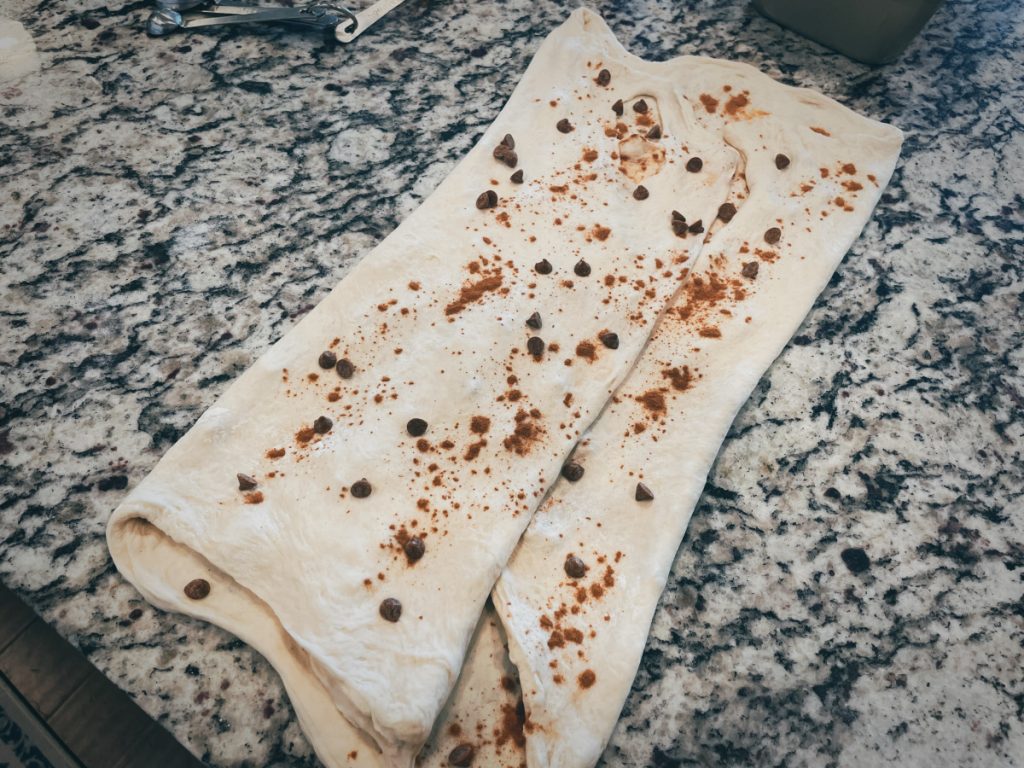 sourdough stretched very thin and folded on a countertop with cinnamon, cardamon, and cinnamon chips sprinkled on top