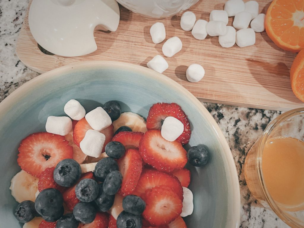 close up of fruit salad in a bowl with marshmallows and honey pot next to it