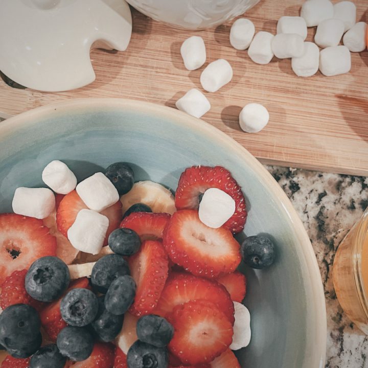 close up of fruit salad in a bowl with marshmallows and honey pot next to it
