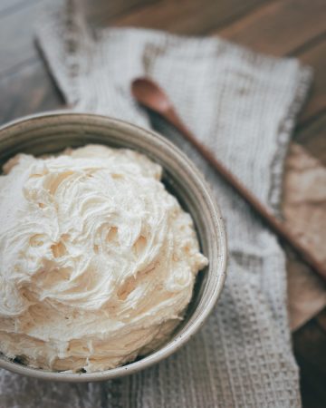 photo of a bowl of buttercream frosting on a linen napkin with a wooden spoon next to it