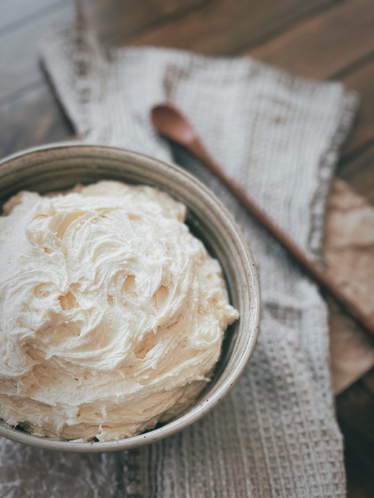 photo of a bowl of buttercream frosting on a linen napkin with a wooden spoon next to it