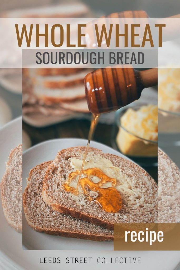 close up of two slices of whole wheat sourdough bread with butter and honey being drizzled on with a honey pot, butter dish, and loaf in the background with the words "whole wheat sourdough bread" overlaid at the top of the image