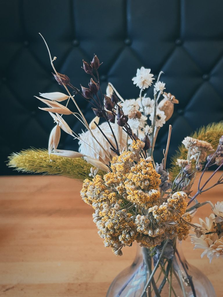clear glass vase with pretty dried flowers sitting on a wooden table with a black backdrop