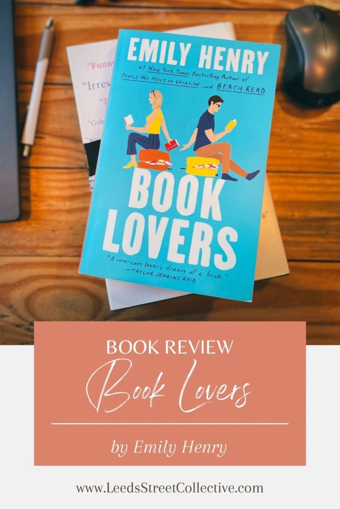 overhead shot of the cover of Book Lovers by Emily Henry sitting on a wooden desk next to a computer, pen, and mouse with the words "Book Review" overlaid