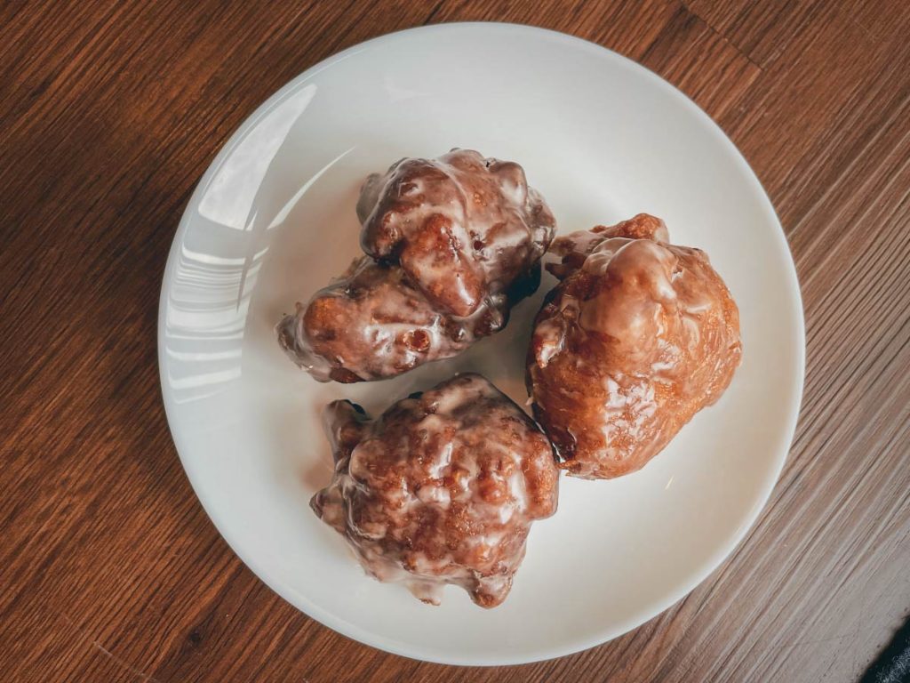 overhead shot of three gluten free apple fritters on a round white plate sitting on a wooden table