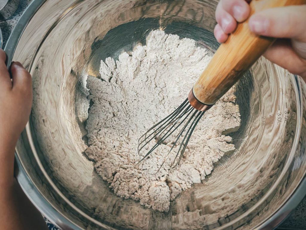 overhead shot of the inside of a silver bowl with gluten free flour being mixed with a whisk