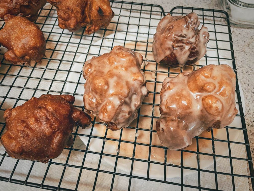 gluten free apple fritters cooling on a wire tray with half of them glazed and half unglazed