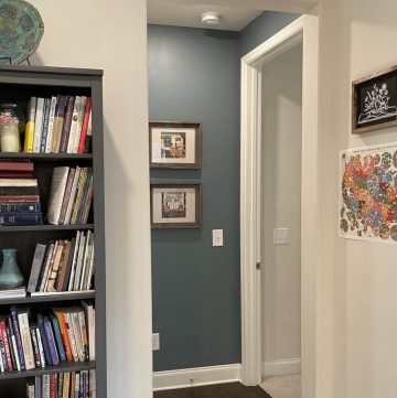 photo of a cozy nook painted blue with 2 framed paintings hung on the wall, next to a gray bookcase