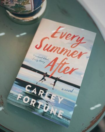 photo of the cover of Every Summer After by Carley Fortune sitting on a teal side table next to a colorful lamp